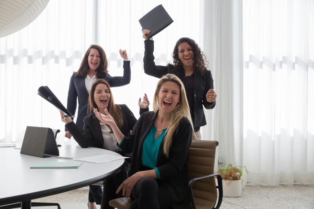 Four women in an office celebrating success and teamwork with enthusiasm.