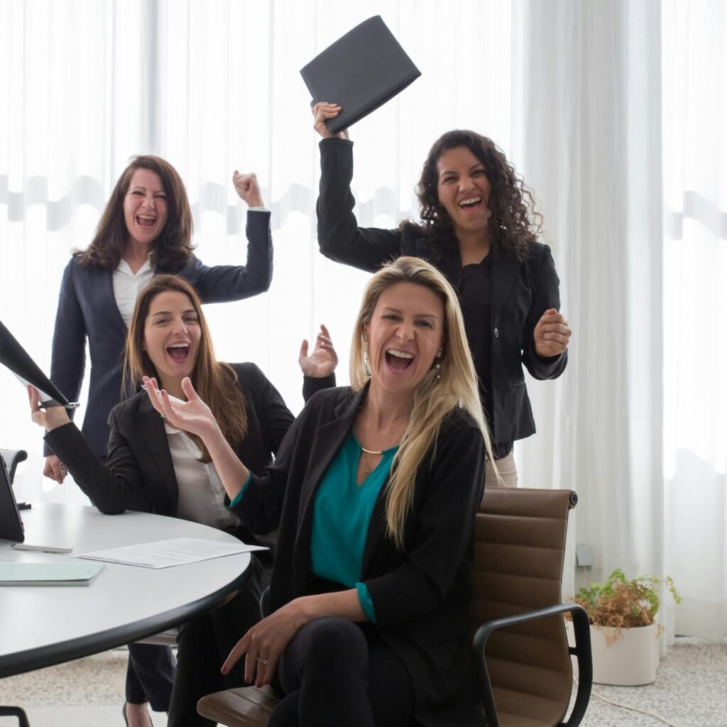 Four women in an office celebrating success and teamwork with enthusiasm.